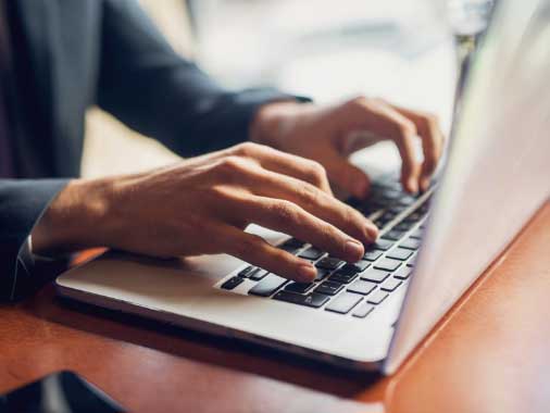 A close up of a man's hands actively typing on a laptop.