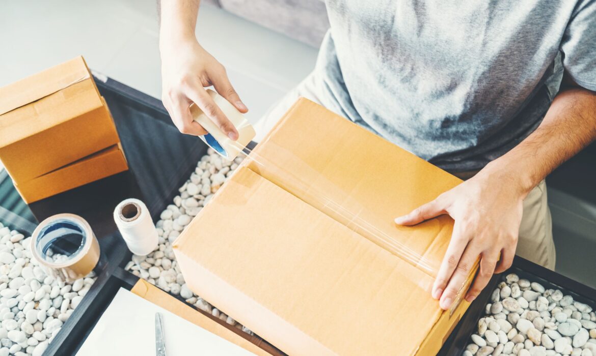 Dynamic Lifecycle Innovations facilitates sustainable takeback programs, shown by a worker sealing boxes amid packaging materials.